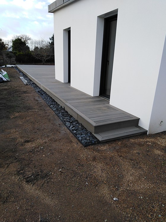 Terrasse composite longeant le pignon de la maison avec bordure en galets de schiste : terrasse longitudinale près de Quimper.