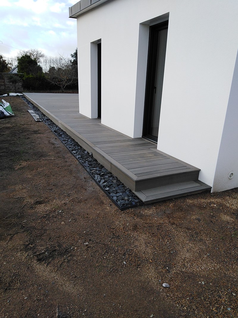 Terrasse composite longeant le pignon de la maison avec bordure en galets de schiste : terrasse longitudinale près de Quimper.